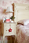 Pink floral patterned bedroom quilt and cream painted bedside table