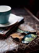 Turquoise teacup on hardback book on leather ripped tabletop
