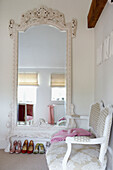 Großer verschnörkelter, weiß gestrichener Spiegel im Schlafzimmer mit Reihen von Schuhen und bemalter Liege