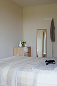 Full length mirror and matching chest of drawers in bedroom with cream double bed cover