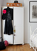 Schwarzes Vintage-Kleid hängt an einem weiß gestrichenen Kleiderschrank im Schlafzimmer