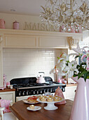 Vase of lilies and cupcakes on stand in country kitchen with pink accessories