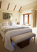 Double bed with white quilt in sunlit cottage bedroom