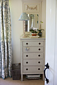 Floral patterned lampshade and curtains with painted chest of drawers