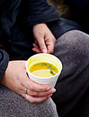 Woman sits holding a cup of soup