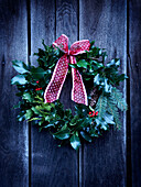 Wreath of holly with red bow on wooden door