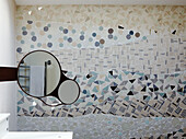 Shaving mirror reflects towel rail in mosaic tiled bathroom 