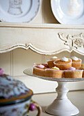 Iced buns on a cake stand and ornate carved kitchen dresser