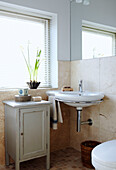Washbasin with painted cabinet in sunlit window of cream tiled bathroom