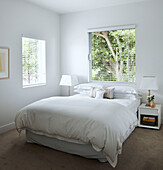 Weiße Bettdecke im Schlafzimmer mit Jalousien an den Fenstern