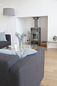 Grey sofa and standard lamp shade with wood burning stove in sustainable housing Gloucestershire