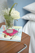 Cut flowers and a book with reading glasses on bedside table 
