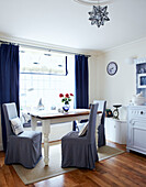 Slip covered dining chairs at sunlit window with curtains and blinds