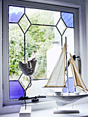 Modellboot und Skulptur am Fenster mit Buntglasscheiben