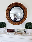 Reflection of living room in convex mirror above shelf with jewel cases and indoor plants