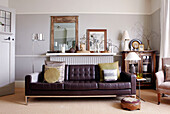 Brown leather sofa with mirrors on radiator shelf in living room of country home