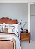 Pfirsichfarbene Kopf- und Fußteile des Bettes mit Winkelpoise-Lampe auf hölzernem Nachttisch