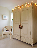 Lit fairy lights on painted cream wardrobe with wicker chair