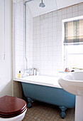 Shower fitting above blue claw foot bath in sunlit bathroom