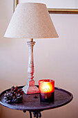 Scented candle and pinecones on side table with lamp