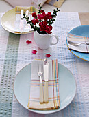 Knives and forks with napkins on plates and cut flowers on table