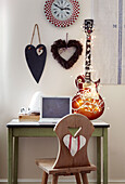 Carved wooden chair at desk with heart shaped wall ornaments and electric guitar