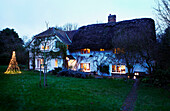 Illuminated Christmas lights in garden of thatched cottage