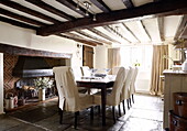 Slip covers on dining chairs at table below beamed ceiling in Forest Row farmhouse Surrey England UK