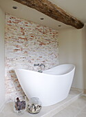 White ceramic freestanding bath and ceiling beam in renovated Cotswolds mill house England UK