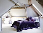 Lila Velours-Bettdecke auf dem Bett im Dachgeschoss eines renovierten Mühlenhauses in den Cotswolds, England, UK