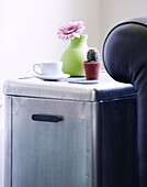 Tasse und Untertasse mit einer einblättrigen Blume und einem gestrickten Kaktus auf einer Aufbewahrungsbox aus Metall in einem Londoner Familienhaus UK