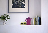 Books and pink coffee pot with vase of cut flowers on alcove shelving in London family home UK