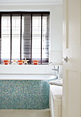 Turquoise mosaic tiled bath below window with louvered blinds in Harrogate home Yorkshire England UK
