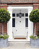 Two potted trees flank white front door of brick porch exterior London home UK
