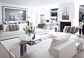 Circular coffee table and modern art in seating area of white mirrored living room in London home UK