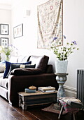 Flower arrangement on vintage plinth with brown leather sofa and wall hanging in living room of London home UK