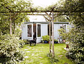 Dog stands outside summerhouse in garden with pergola London UK