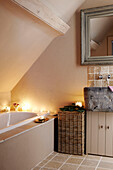 Large mirror over stone washbasin wit candlelit bath in festive Oxfordshire home, England, UK