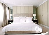 Master bedroom with white duvet and matching dar wood bedside tables in London home, England, UK