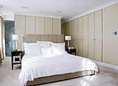Master bedroom with dark wood bedside tables and wall partition to ensuite bathroom in luxury London home, England, UK