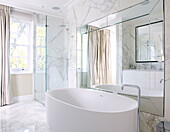 Freestanding bath in marble bathroom with large mirror reflecting light, London home, England, UK