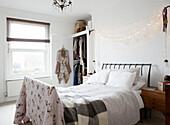 String of lights above unmade bed with grey checked blanket and floral quilt in contemporary home, Hastings, East Sussex, UK