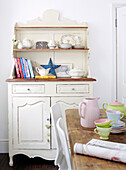 Pastel coloured crockery on kitchen table with painted dresser in Greenwich home, London, UK