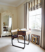Antique wooden desk at window of bedroom with mirrored wardrobe in Warwickshire home, England, UK