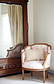 Upholstered antique armchair with mirrored wardrobe in Warwickshire home, England, UK