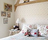 Kunstwerk an einer Schlafzimmerwand mit blumenbestickten Kissen und Nachttisch in einem Bauernhaus in Oxfordshire, England, Vereinigtes Königreich