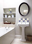 Tiled splashback and oval mirror above pedestal basin with recessed shelving in Oxfordshire home, England, UK