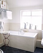 Krüge auf der Fensterbank in einem cremefarbenen und weißen Badezimmer mit antikem Waschtisch in einem Haus in Staffordshire, England, UK