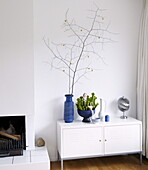Zweigarrangement und Zimmerpflanzen mit Ornamenten auf weißem Sideboard in einem Haus in Bussum, Niederlande