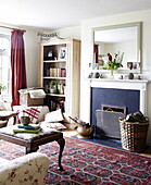 Brennholz und Bücherregal im Wohnzimmer mit gemustertem Teppich und Spiegel über dem Kamin, Oxfordshire, England, Vereinigtes Königreich